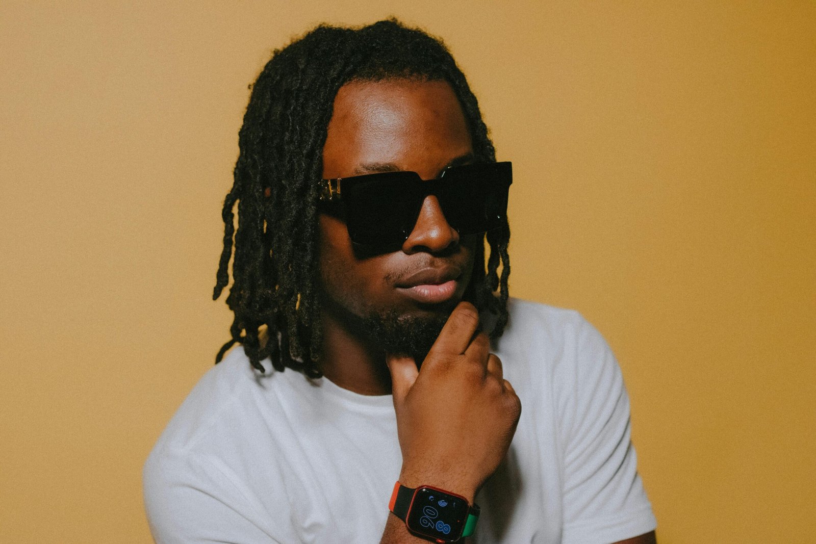 Portrait of a fashionable man with sunglasses and smartwatch against a yellow backdrop.