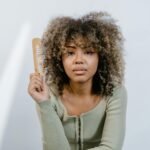 Portrait of a woman with natural afro hair holding a wooden comb, emphasizing beauty routines.