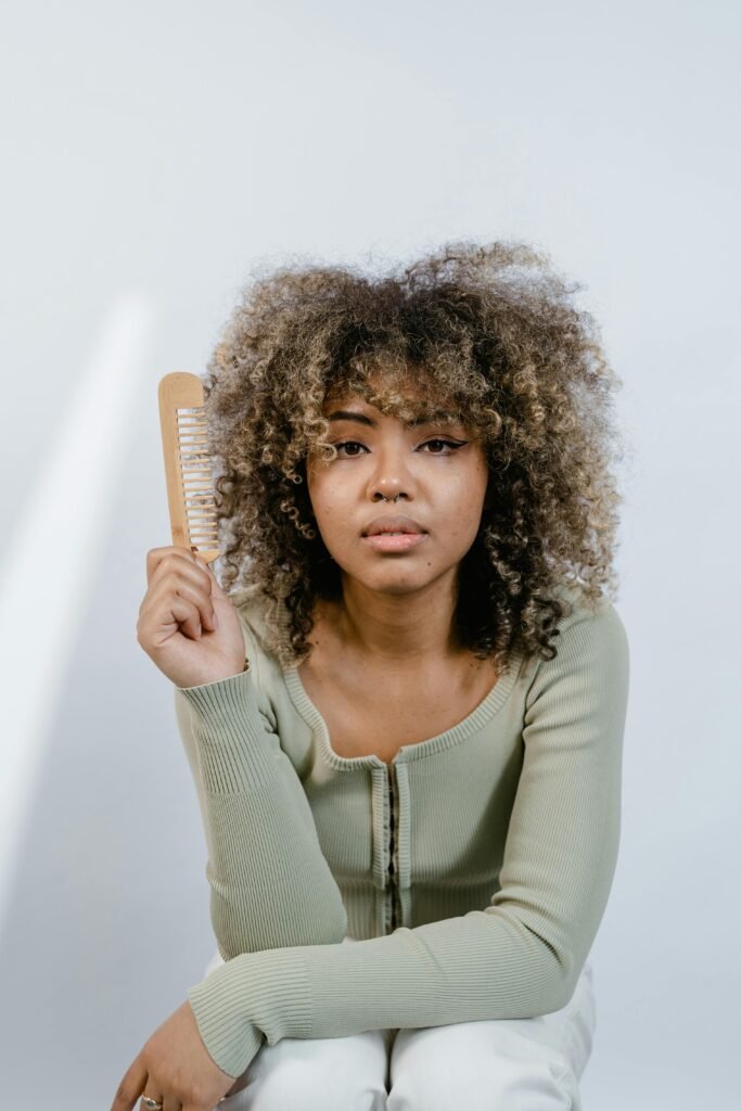 Portrait of a woman with natural afro hair holding a wooden comb, emphasizing beauty routines.