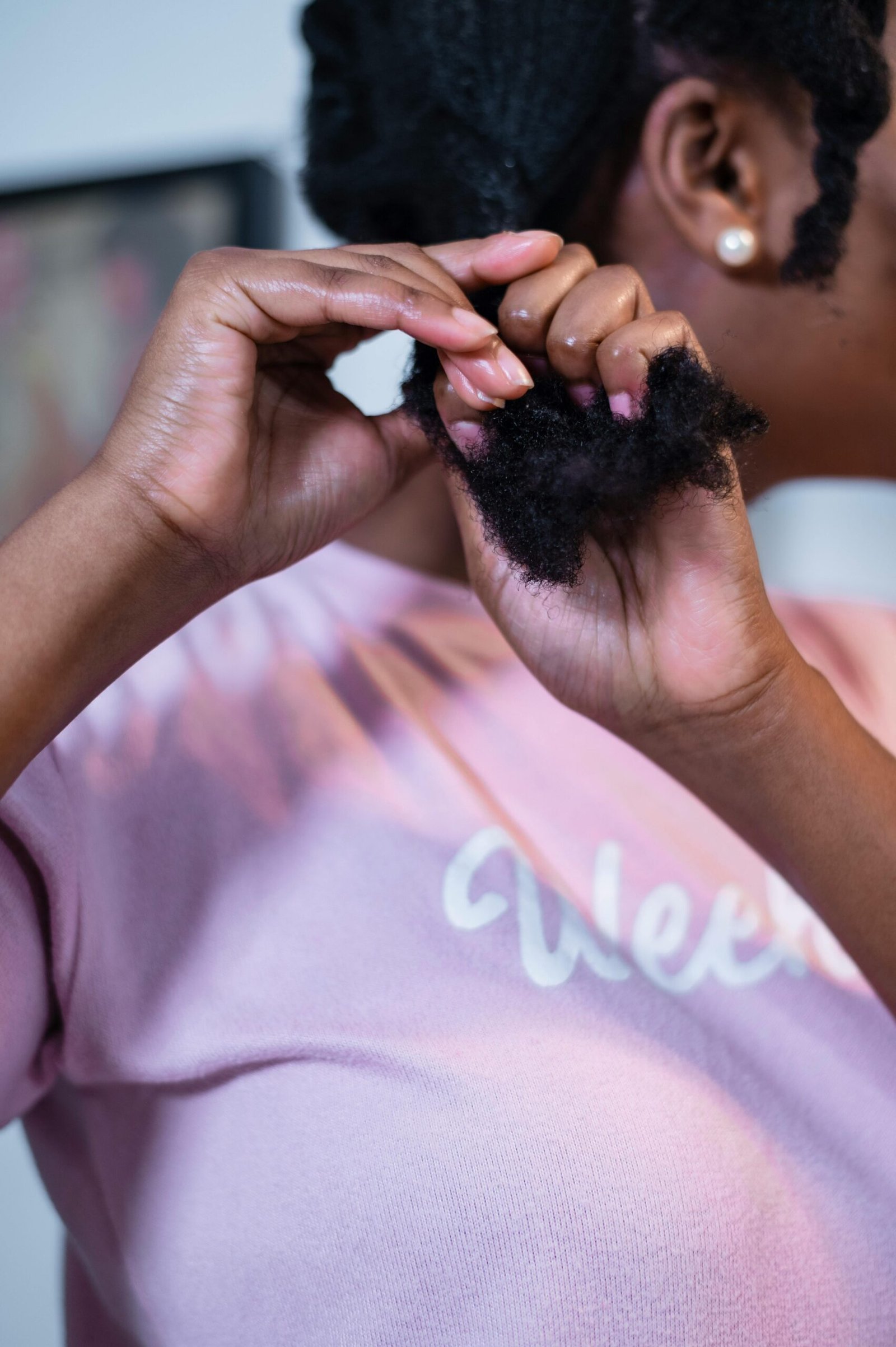 Detailed view of a woman styling her curly hair indoors, focusing on personal care.